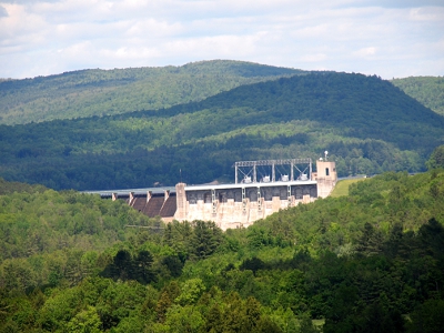 [A sand colored structure rises out of the trees in the foreground. In the background are several layers of the Green Mountains.]